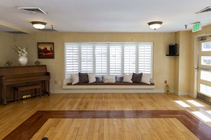 A cozy living room with a large window seat, hardwood flooring, and a piano.