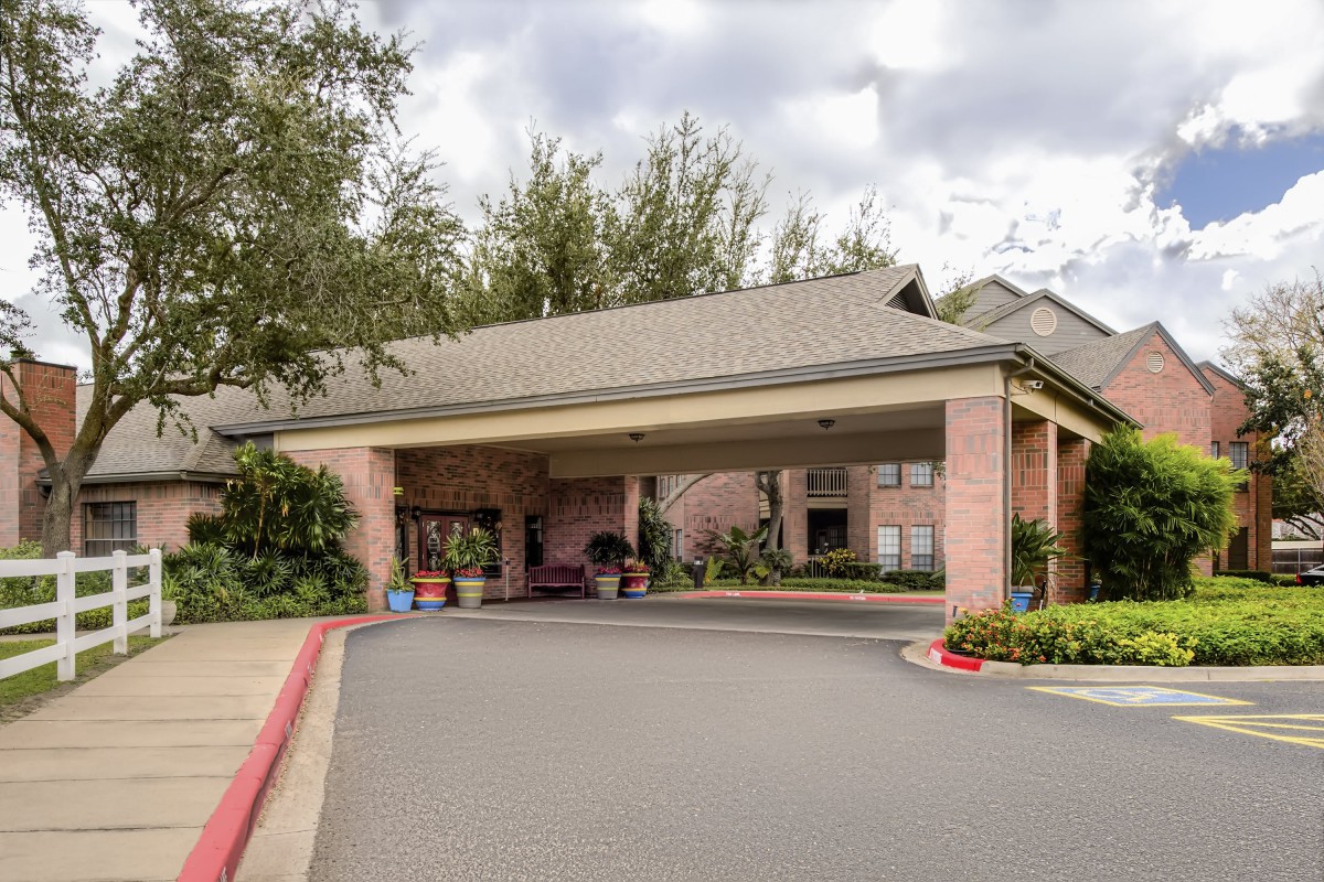 A building entrance with a covered driveway surrounded by trees and landscaping on a cloudy day.