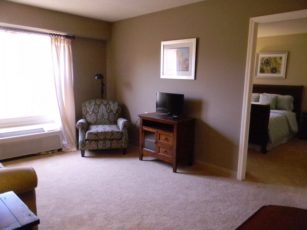 A cozy living room with a patterned chair, small TV on a wooden stand, and natural light from the window.