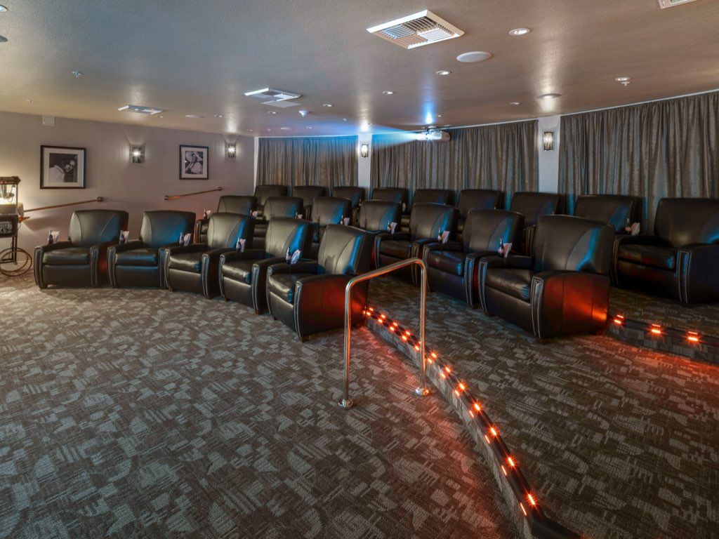 A cozy home theater with rows of leather recliners and a large projector screen.
