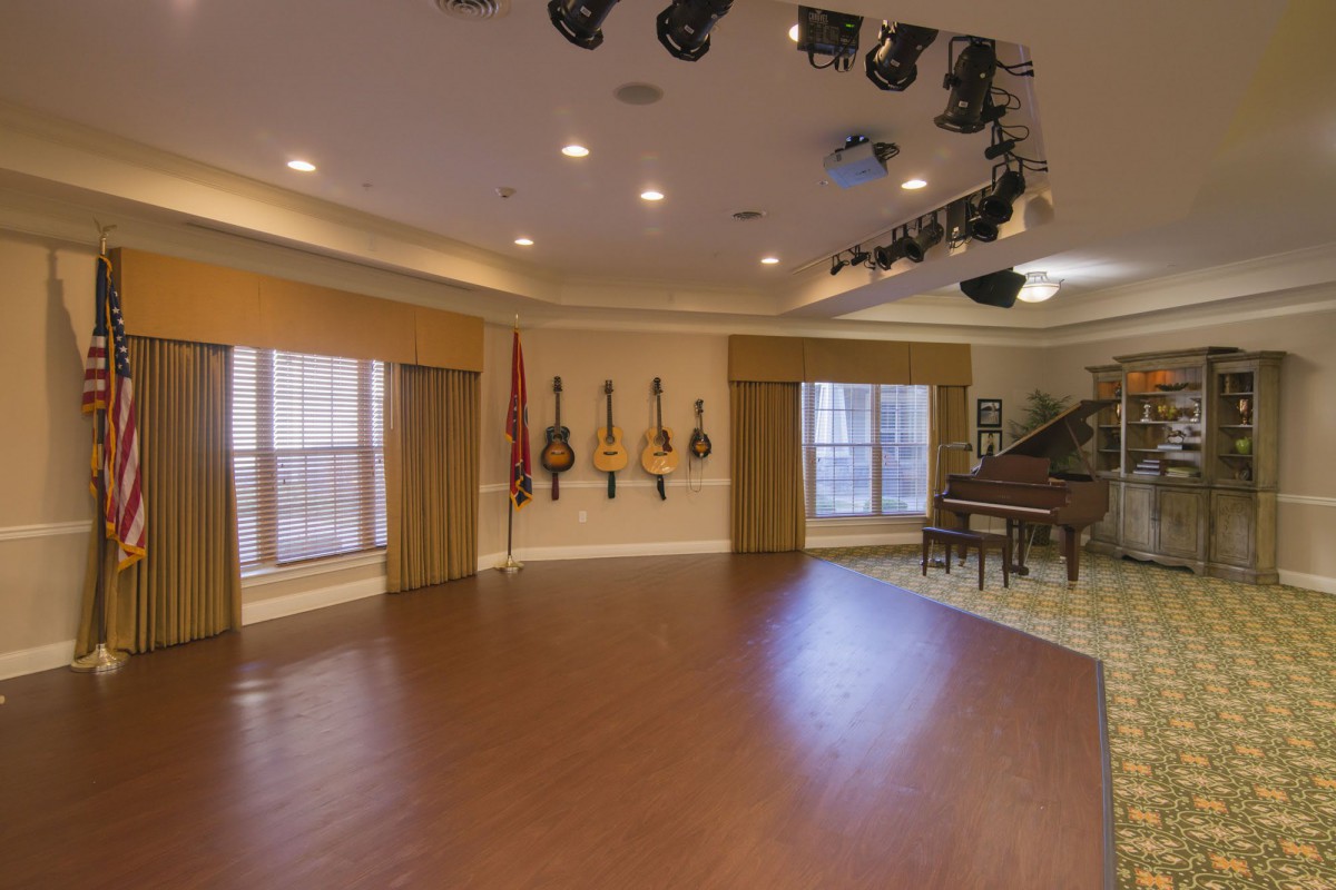 A spacious music room featuring various string instruments and a grand piano, with spotlights overhead.