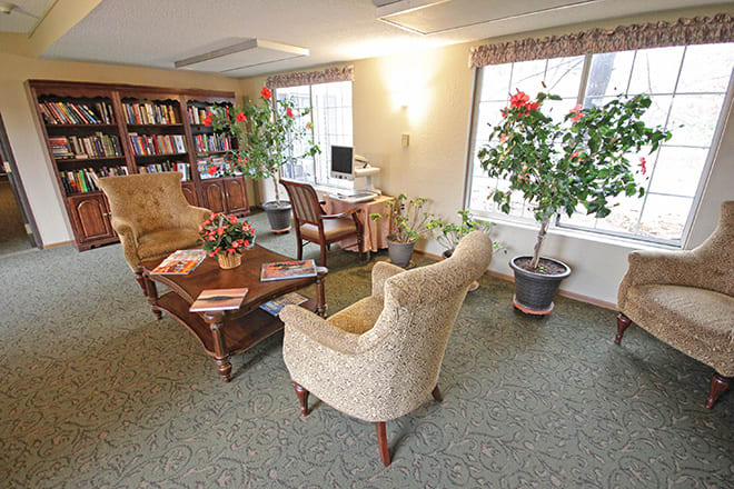 A cozy living room with bookshelves, comfortable chairs, and potted plants.
