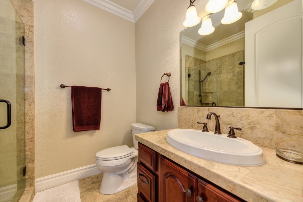 A well-lit bathroom featuring a sink, mirror, and toilet with decorative towels.