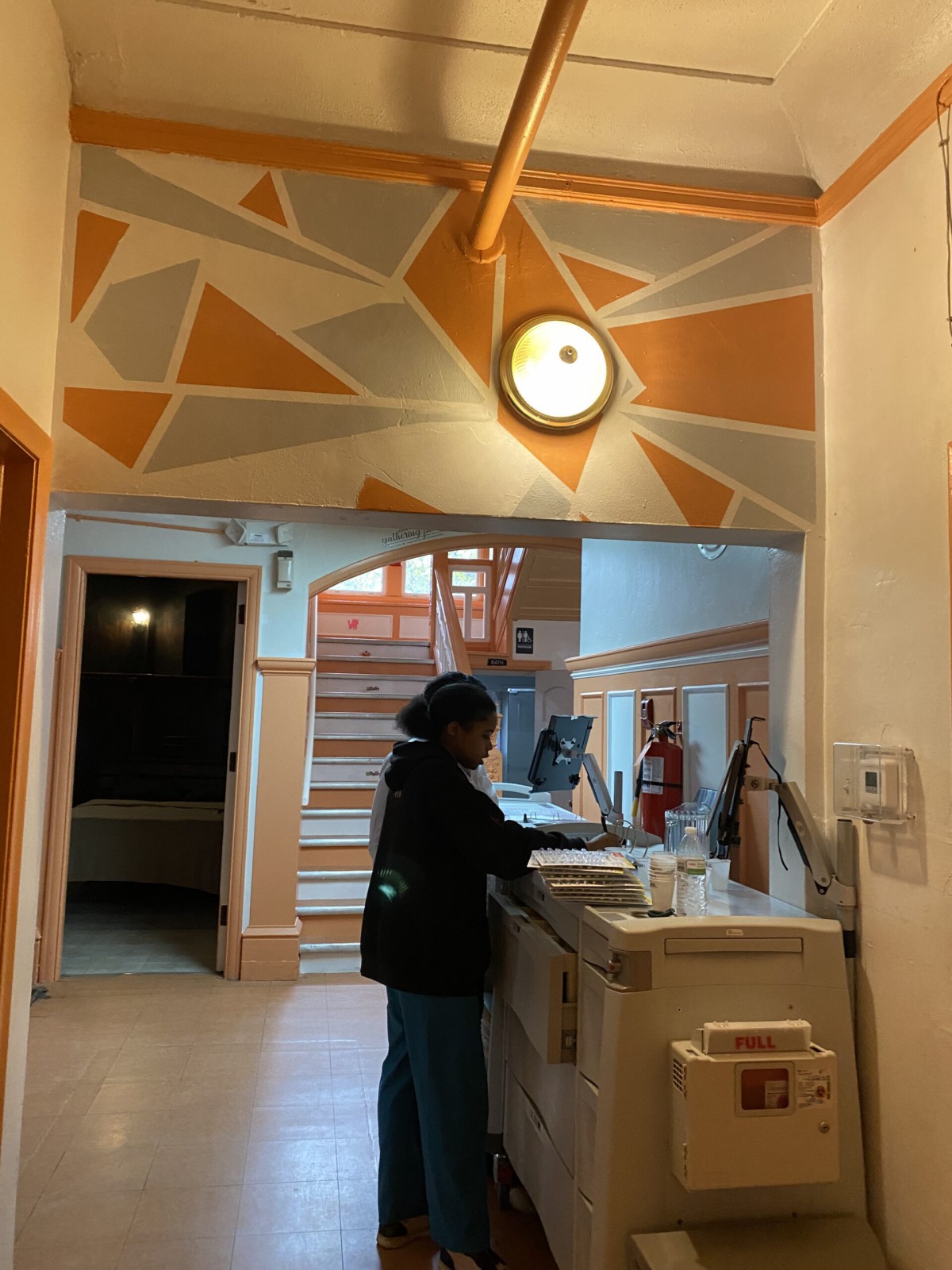 A person stands at a reception desk with abstract wall art and a clock above.