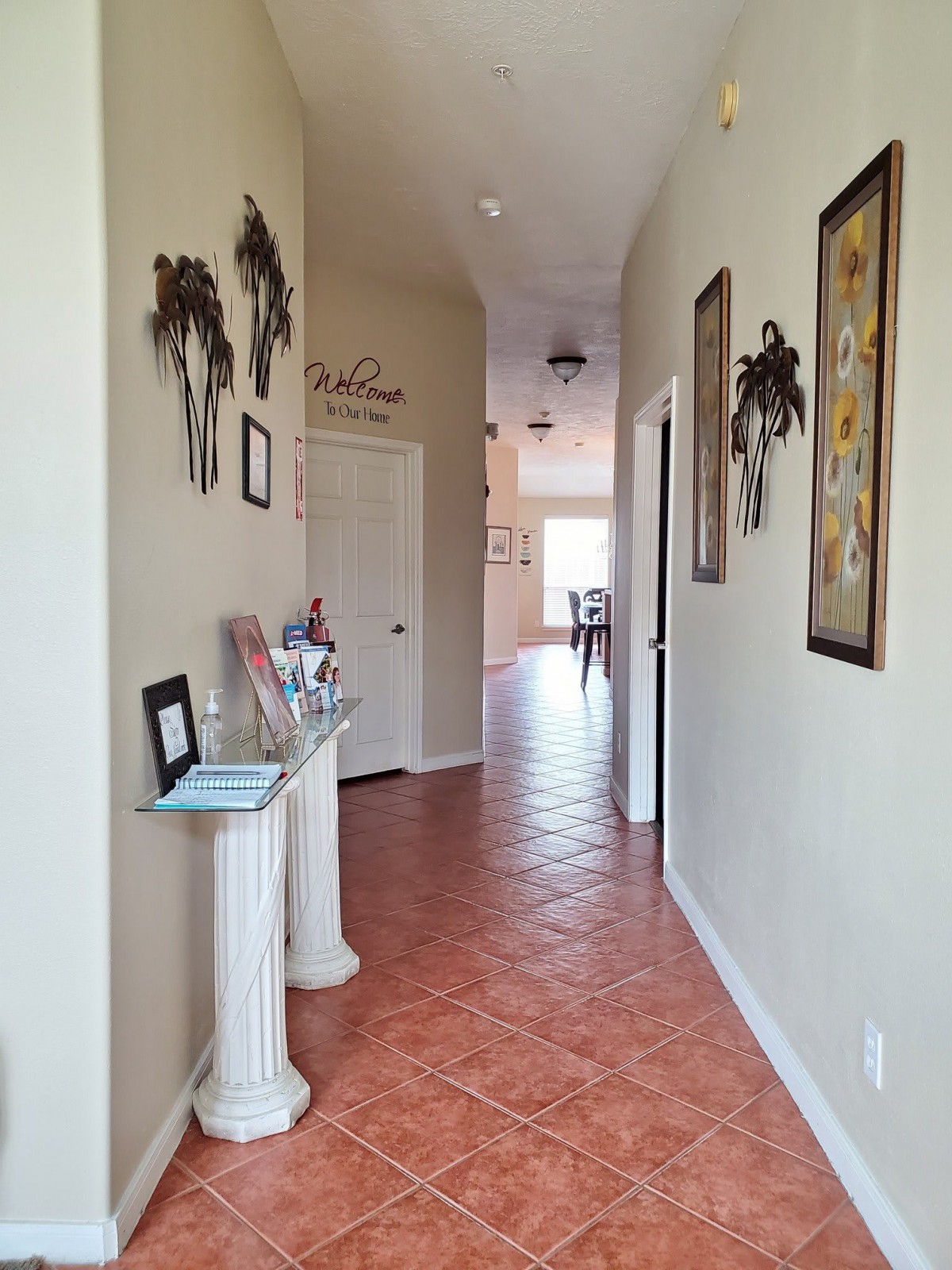 A decorated hallway with tile flooring, featuring wall art and a small console table.