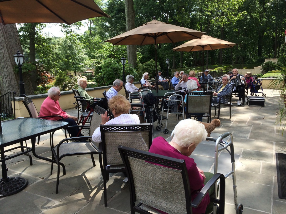 A group of elderly individuals sitting outdoors on a patio, enjoying a sunny day under large umbrellas.