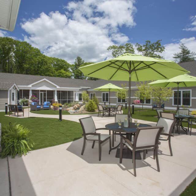 A tranquil patio area with tables, chairs, and green umbrellas in a landscaped residential setting.