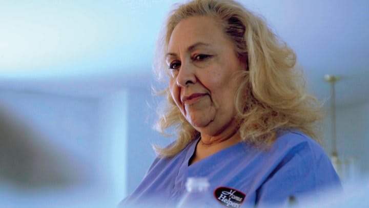A woman in a light blue uniform is smiling softly indoors.
