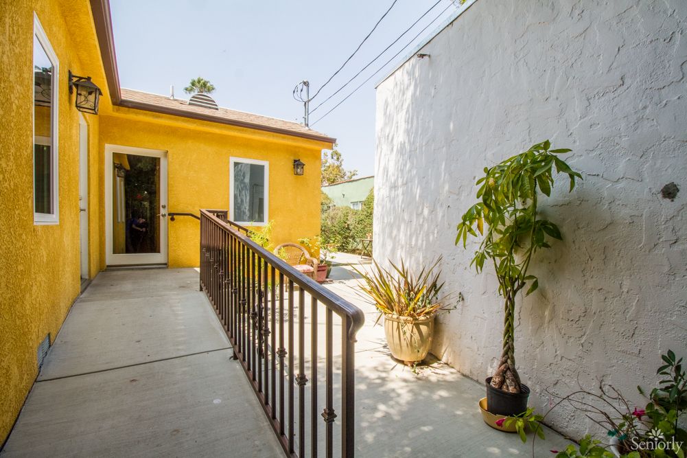 A sunny patio with a yellow exterior wall, potted plants, and a ramp with railings.