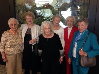 A group of women posing together indoors, wearing formal attire.