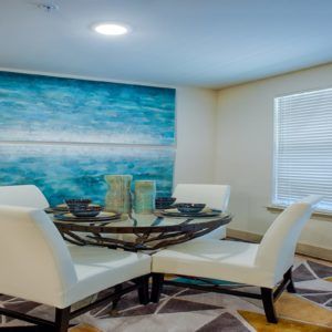 A modern dining room with a glass table and white chairs, featuring a large decorative painting on the wall.