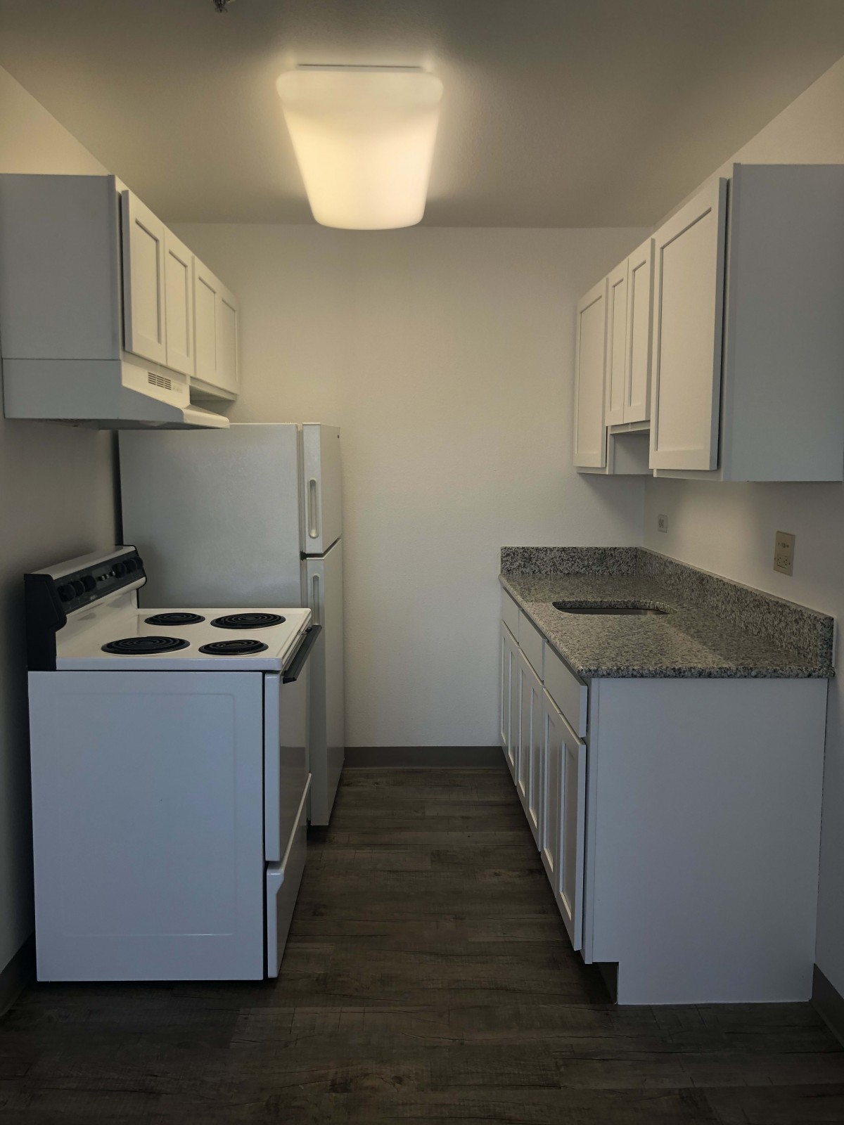 A compact apartment kitchen with white cabinets and modern appliances.