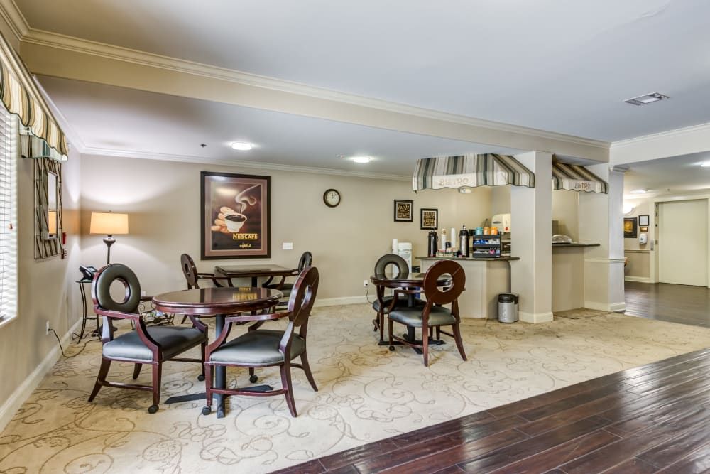 A cozy dining area with multiple tables and chairs, featuring artwork on the walls and a mix of carpet and hardwood flooring.