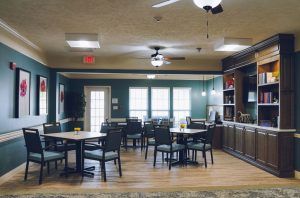 A cozy dining area with several tables and chairs, wooden flooring, and a ceiling fan.