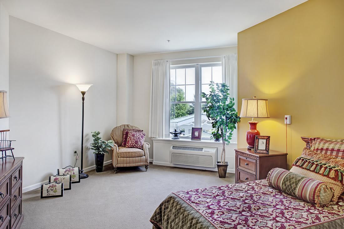 A cozy bedroom with a large window, featuring a bed, chair, and stylish decor.