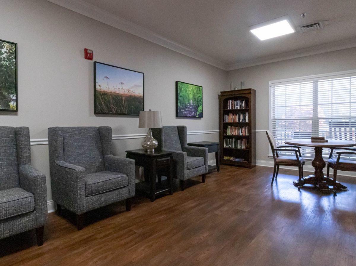A cozy waiting area with comfortable seating, a bookshelf, and large paintings on the wall.