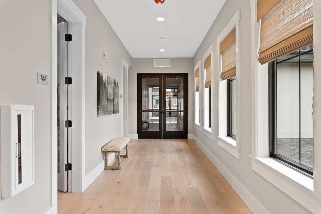 A modern hallway with wooden floors, large windows, and a simple bench.