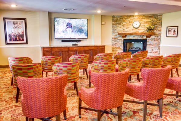 A cozy conference room with arranged chairs facing a large television and a fireplace.