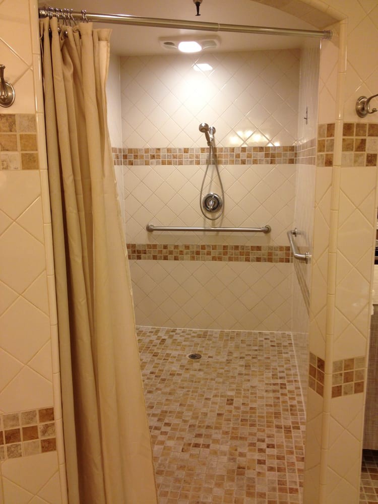 A tiled walk-in shower with a handheld showerhead and grab bar.