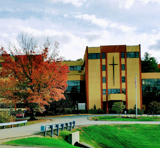 A modern architectural structure with a cross, surrounded by autumn foliage.