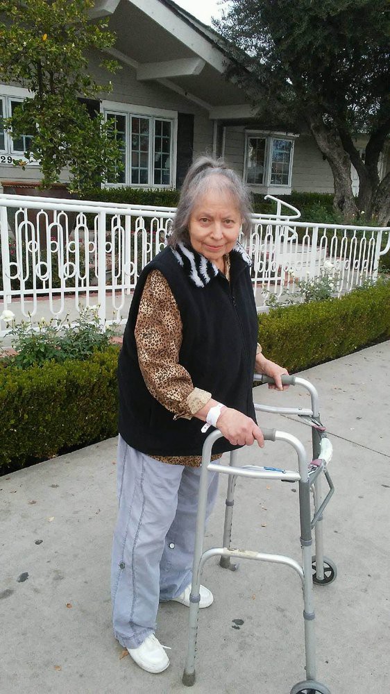 An elderly woman using a walker on the sidewalk.