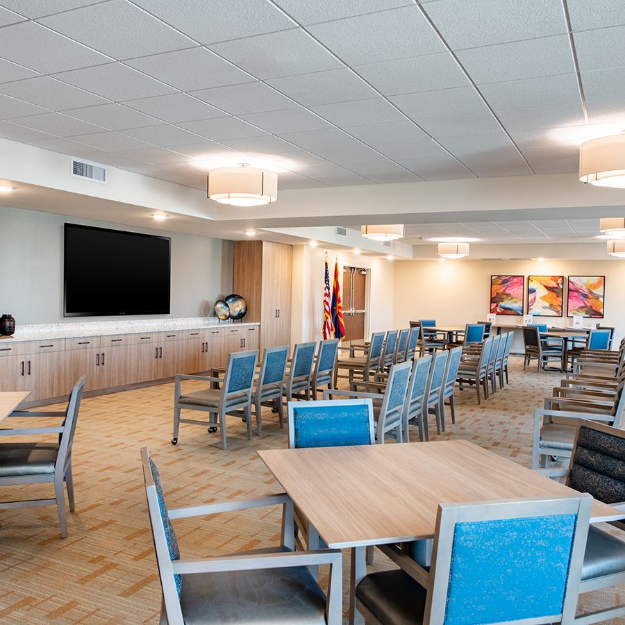 A modern meeting room with blue chairs, tables, and a large television screen on the wall.