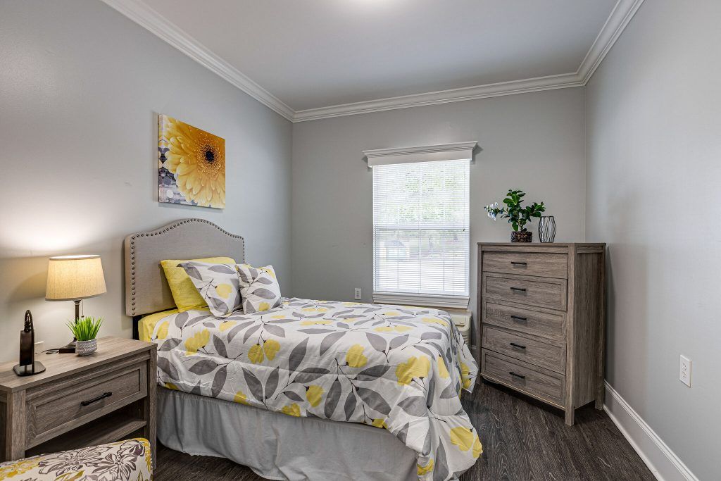 Cozy bedroom with a bed featuring floral-patterned bedding, a dresser, and a flower painting on the wall.