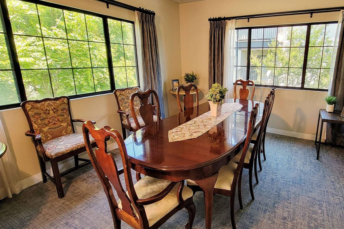 A well-furnished dining room with a large wooden table and chairs surrounded by windows.