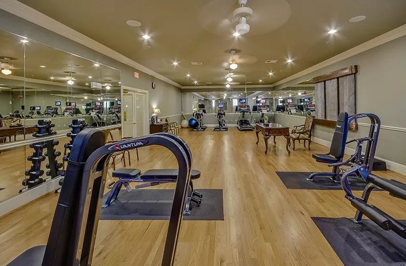 A spacious indoor gym with fitness equipment and mirrored walls, featuring a wooden floor.