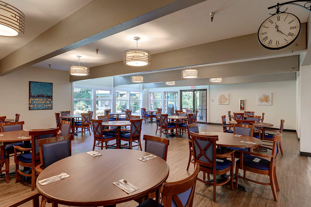 An empty dining area with neatly arranged tables and chairs, featuring modern lighting and a view of the outdoors.