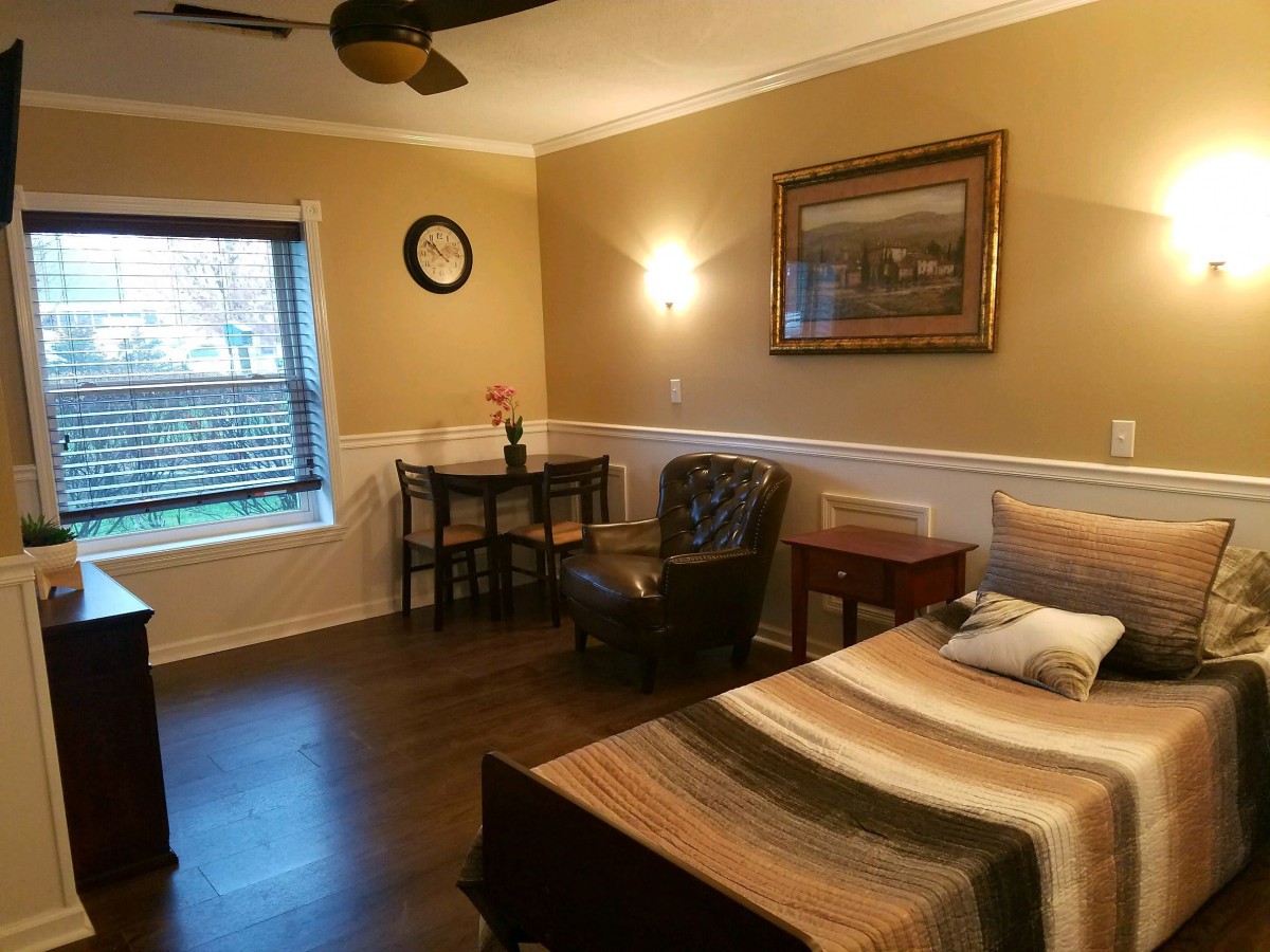 A cozy bedroom featuring a bed, armchair, small table with chairs, and wall decorations.
