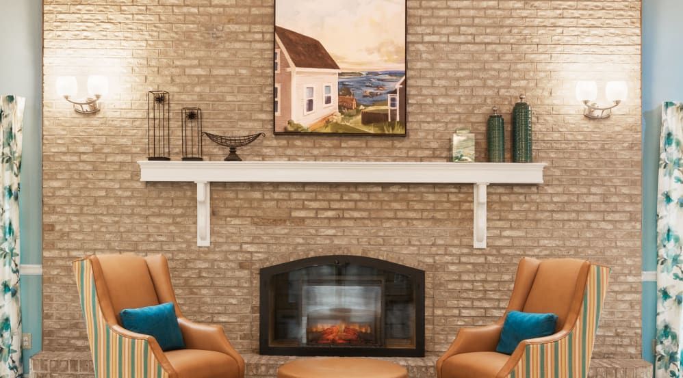 A cozy living room features a brick fireplace adorned with artwork and elegant decorations, surrounded by comfortable seating.
