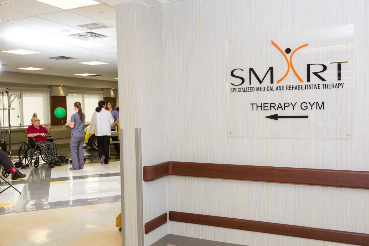 A hospital hallway with a sign pointing to the therapy center and people in the background.
