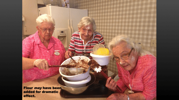Three elderly women having fun baking together in the kitchen.