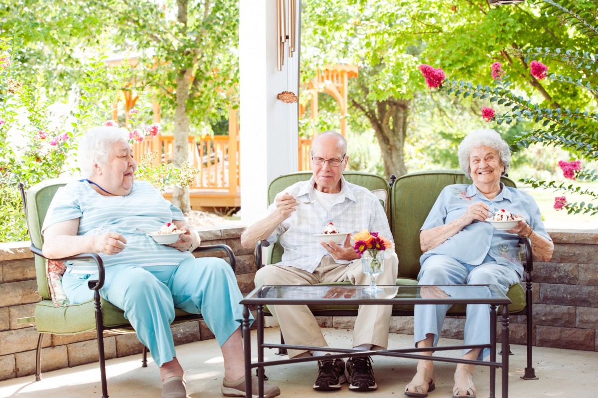 A group of seniors enjoying a relaxed conversation while sitting outdoors in a garden setting.