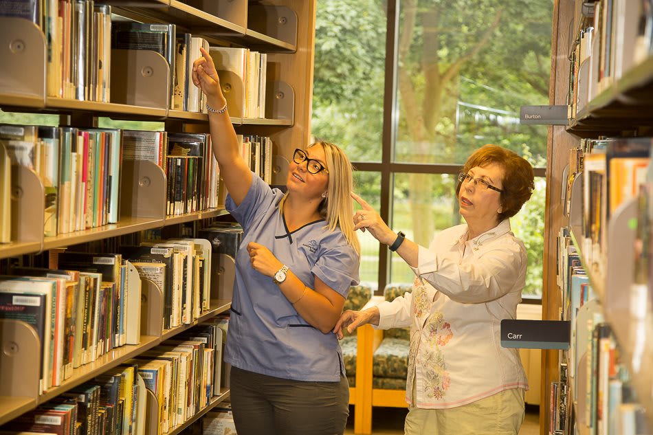 Two women looking at books on a library shelf.