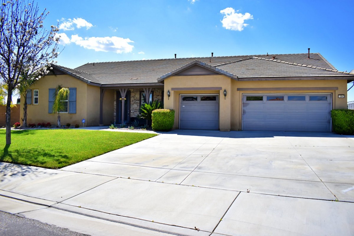 A single-story suburban house with a well-maintained front yard and a spacious driveway under a clear blue sky.