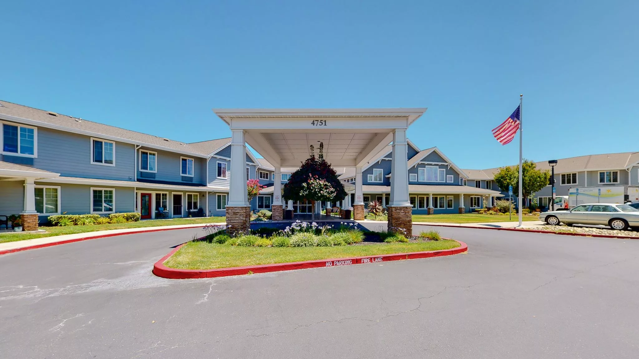 A large building entrance with a driveway and landscaped greenery.