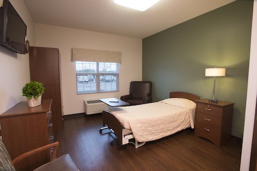 A clean and simple hospital room with a bed and basic furniture.
