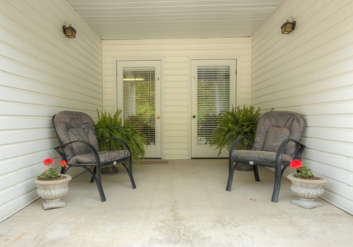 A cozy porch with two cushioned chairs and potted plants, perfect for relaxation.