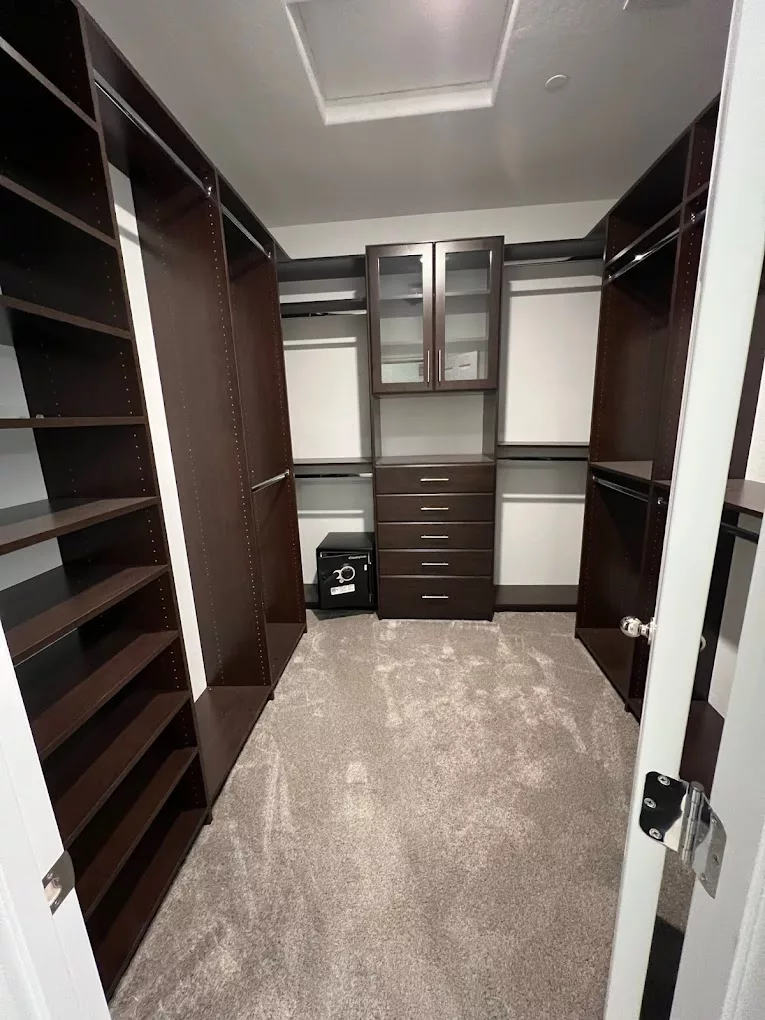 A spacious walk-in closet with dark wood shelving and drawers for organized storage.