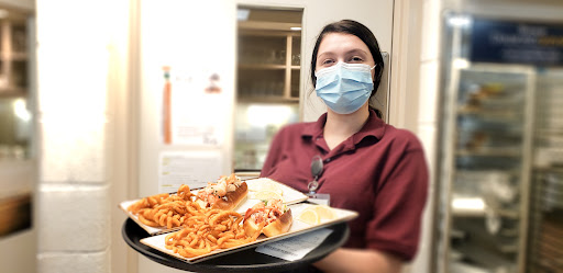 A staff member in a mask serving hot dogs and fries on a tray.