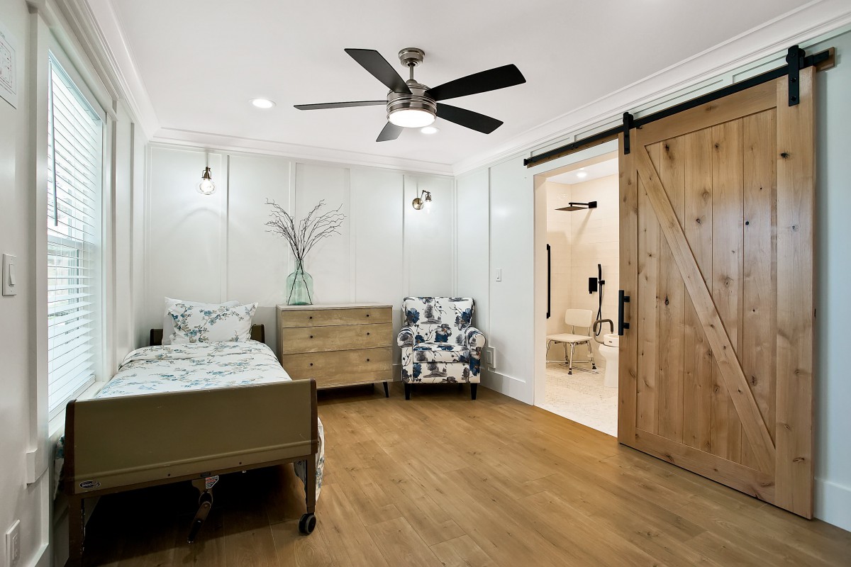 A modern bedroom featuring a ceiling fan, a sliding barn door, and wood flooring.