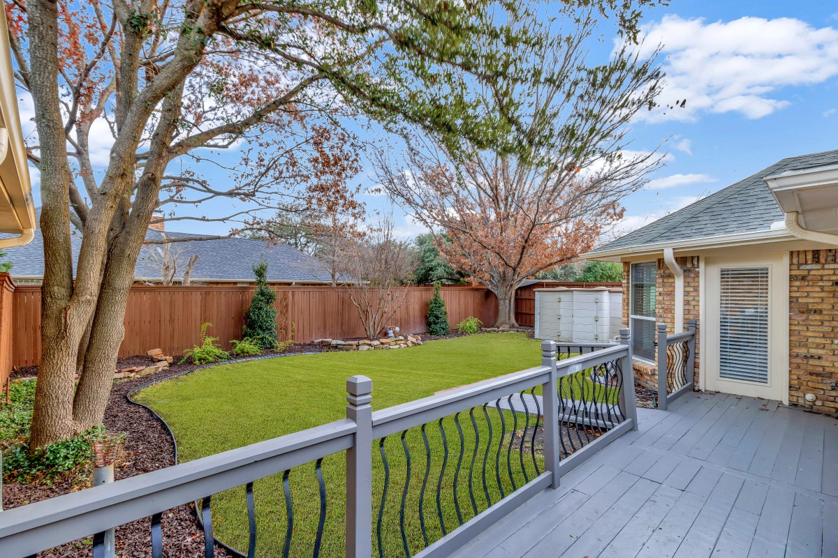 A peaceful backyard with a wooden deck overlooking a green lawn and trees.