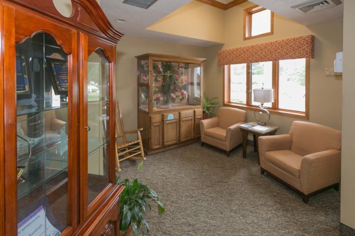 A cozy living room area with armchairs, a cabinet, and a large window allowing natural light.