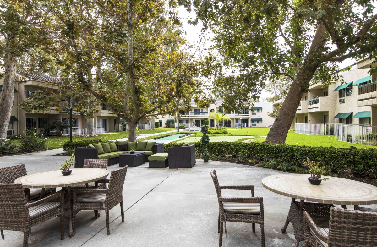 A tranquil outdoor patio with tables and chairs surrounded by lush greenery and trees.