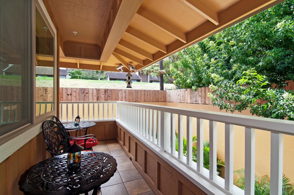 A cozy balcony with seating and a view of lush greenery.