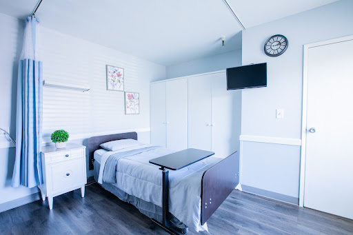 A clean and organized hospital room featuring a single bed, bedside table, television, and simple decor.