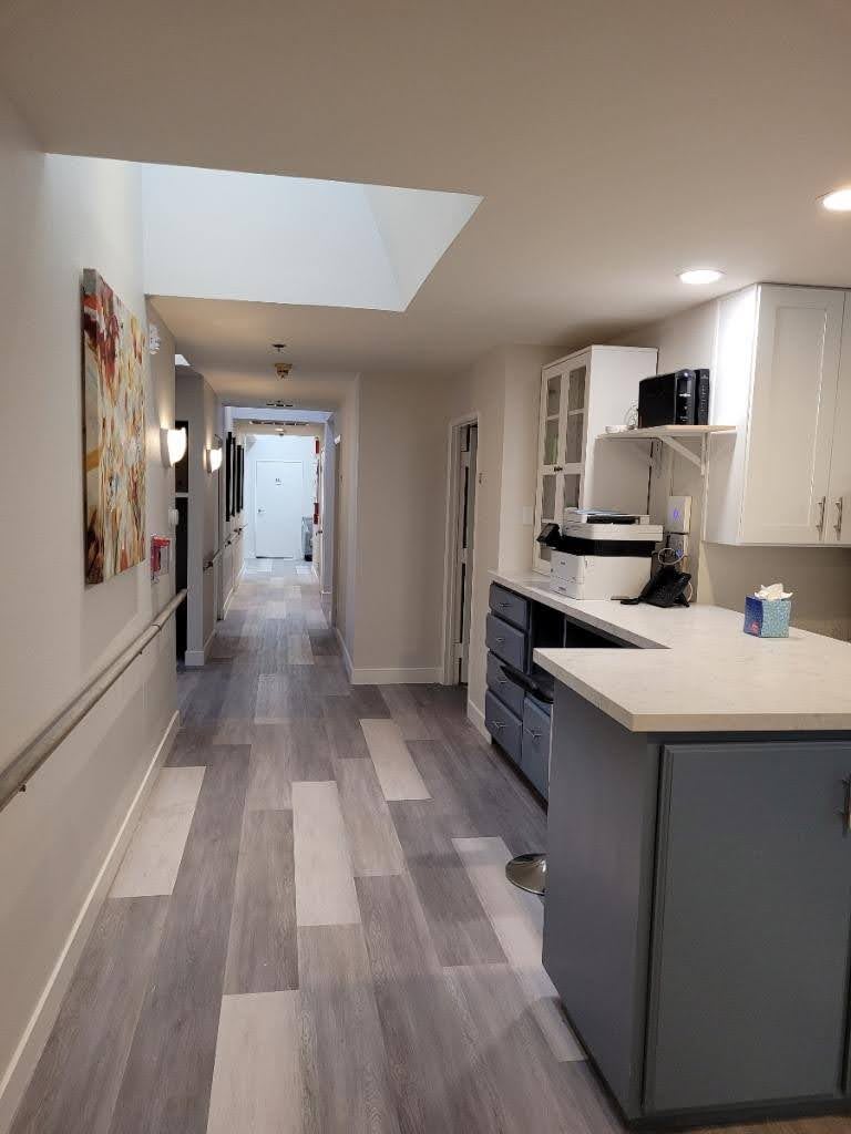 A modern interior hallway with a kitchenette, featuring white cabinets and wood flooring.