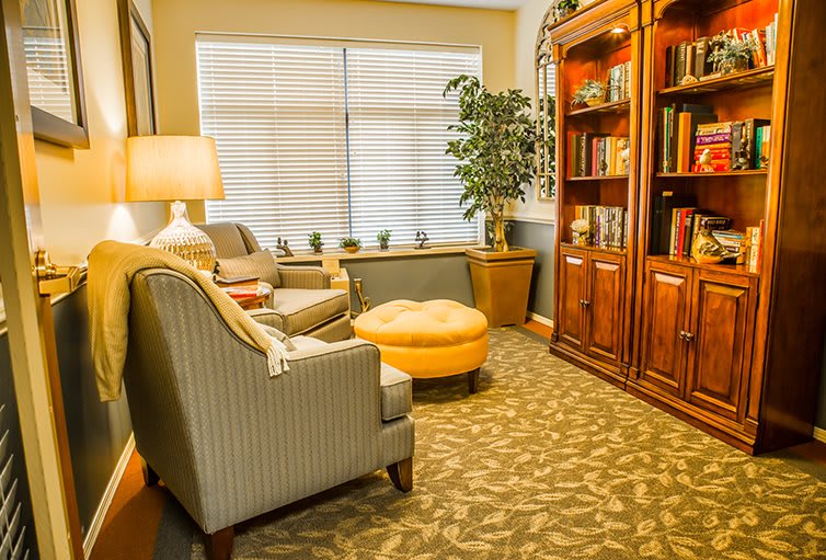A cozy living room with an armchair, ottoman, and a large wooden bookshelf filled with books.